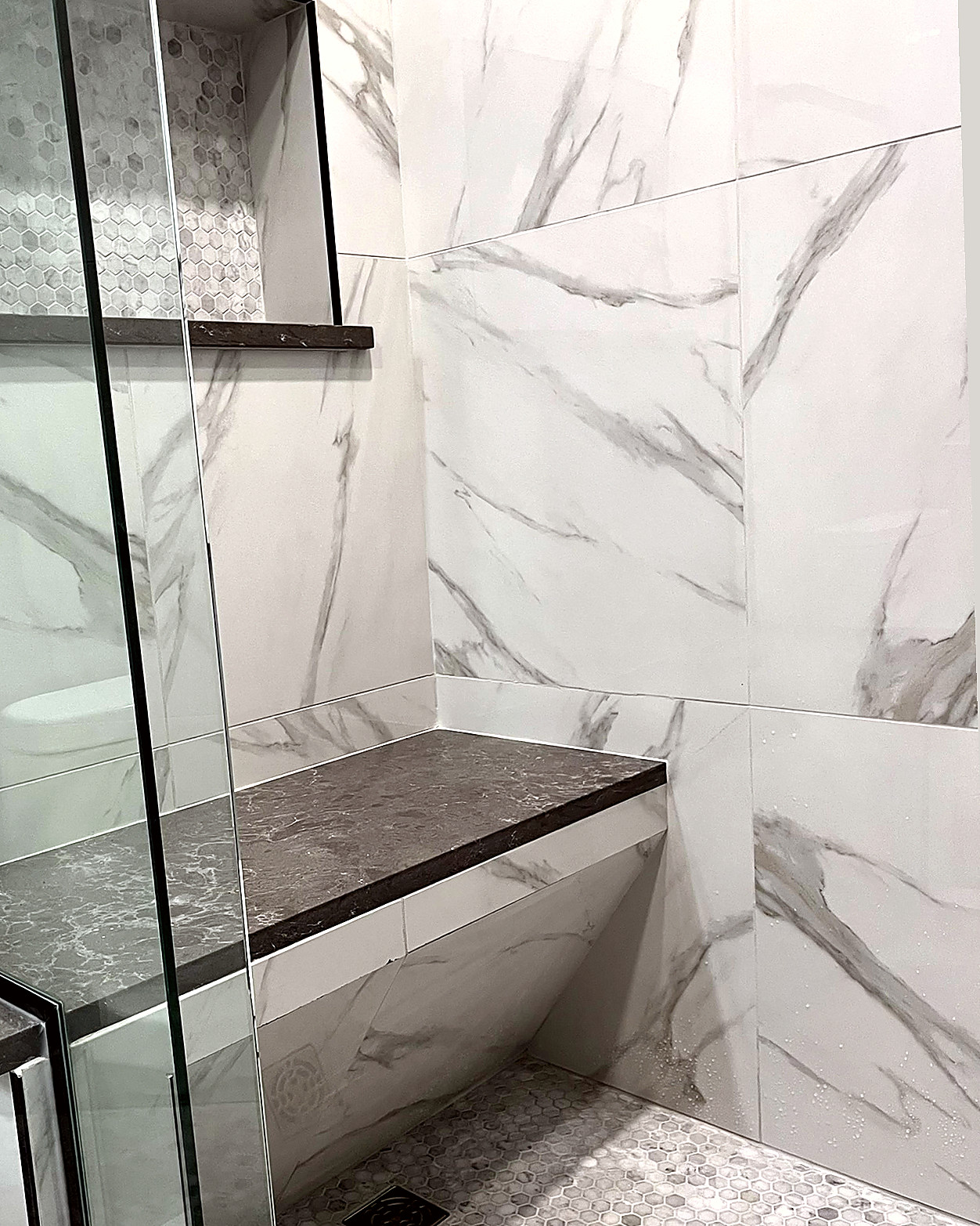 Shower with beige wall tile, a mosaic floor, a tiled bench, and a clear glass panel.