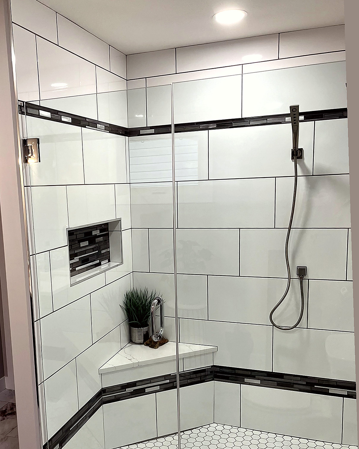 Close view of a shower wall with a horizontal mosaic accent band in beige tile.