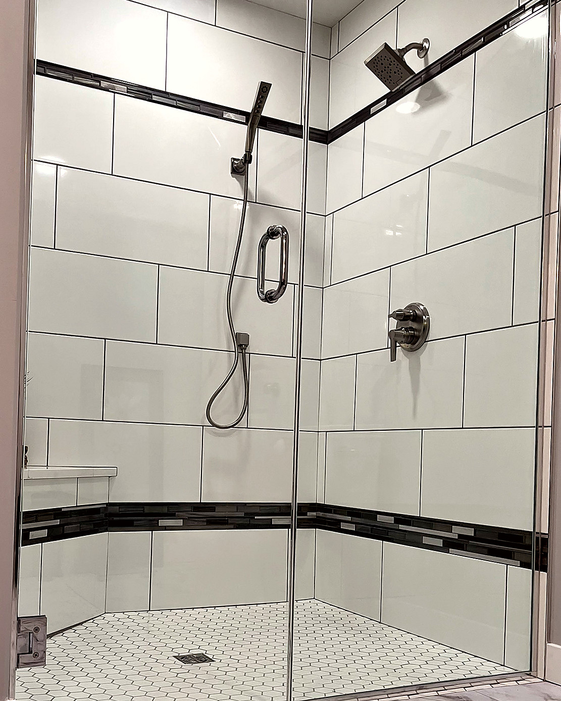 Second view of a beige shower wall with a mosaic accent band and a corner shelf.