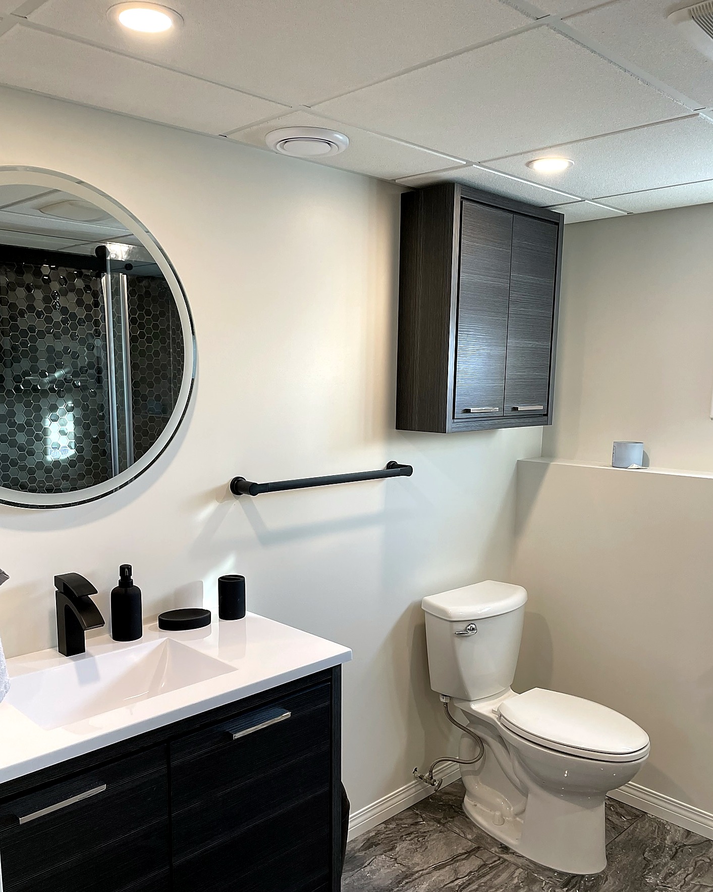 Dark wood vanity with a white counter, round backlit mirror, and black faucet.