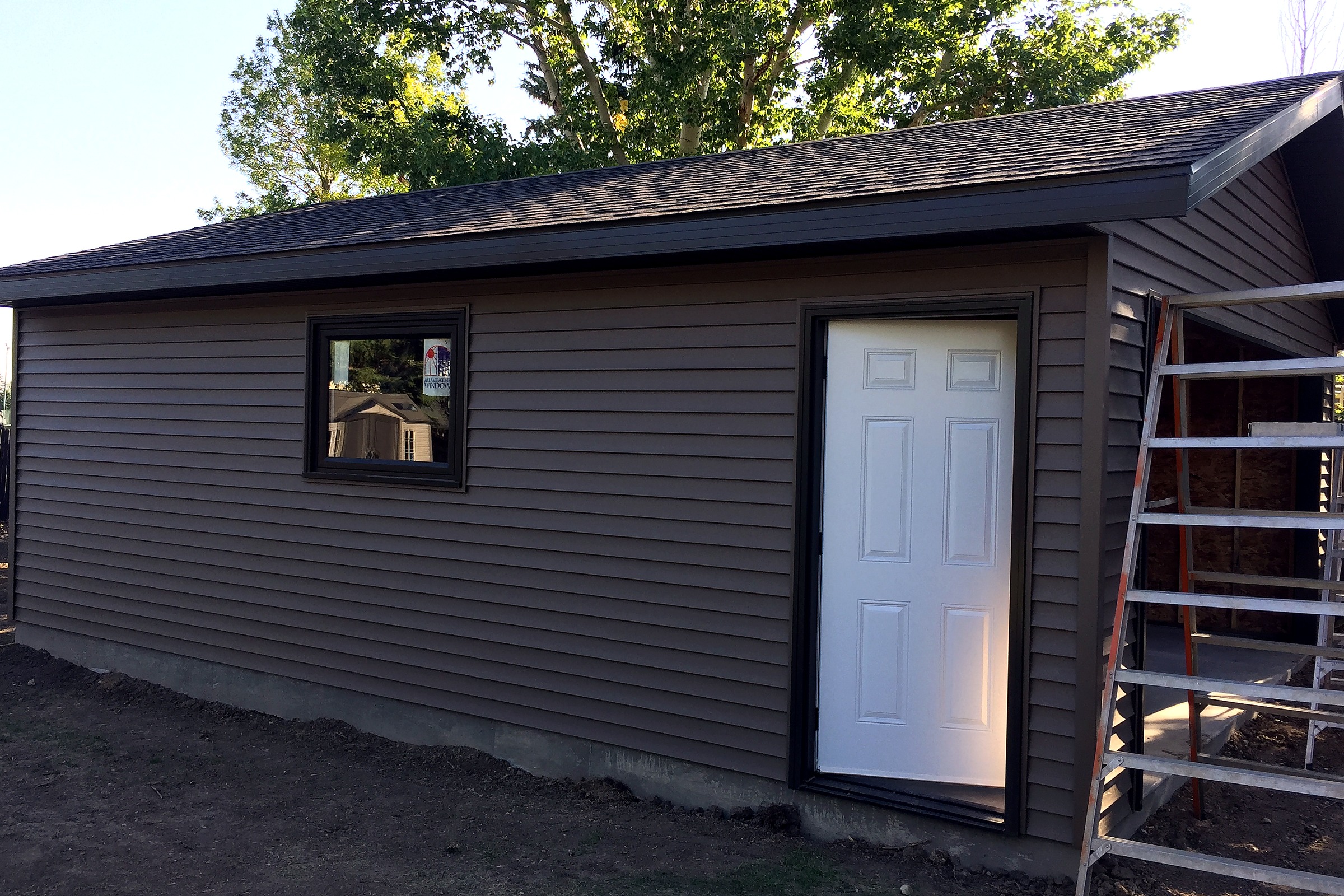 Detached garage at dusk with dark horizontal siding, stone accents, and a paved approach.