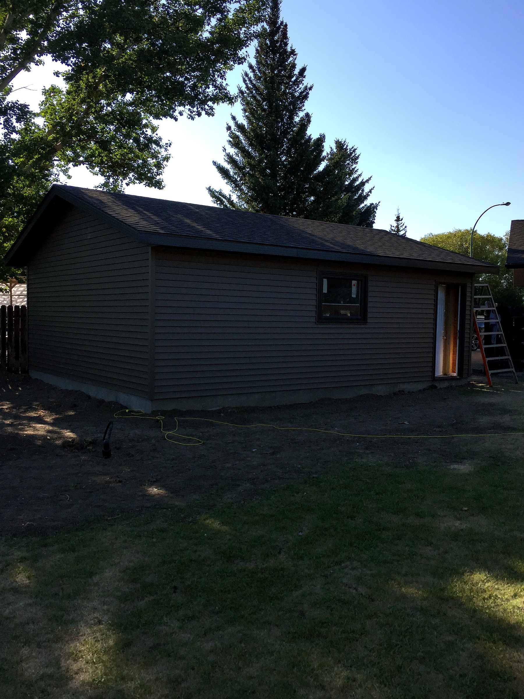 Front of a detached garage with dark siding, a stone veneer column, and a black-framed window.