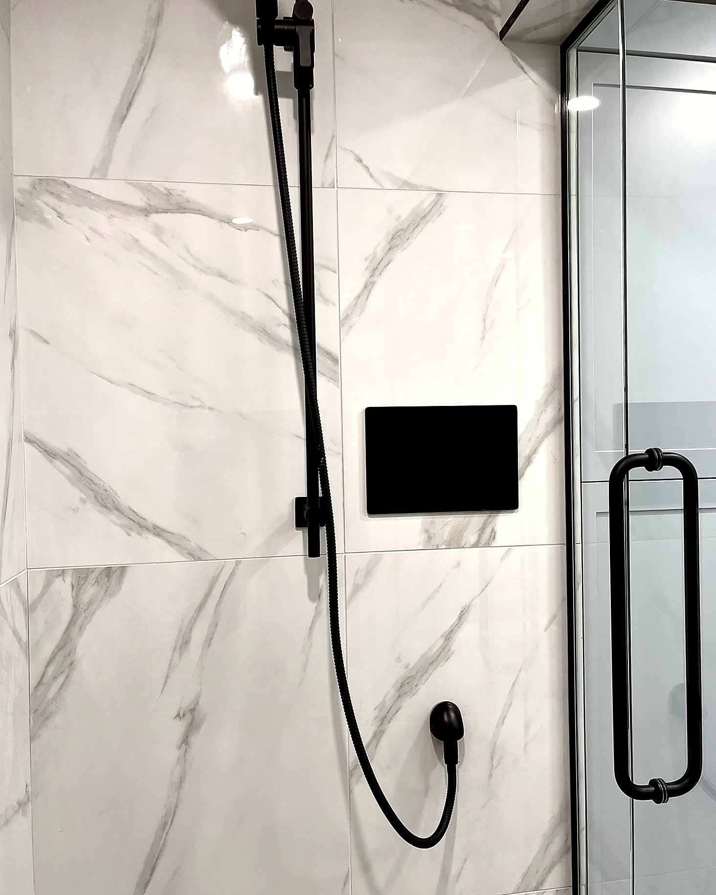 Walk-in shower with large marble-pattern tile and matte black shower head, valve, and hand sprayer.