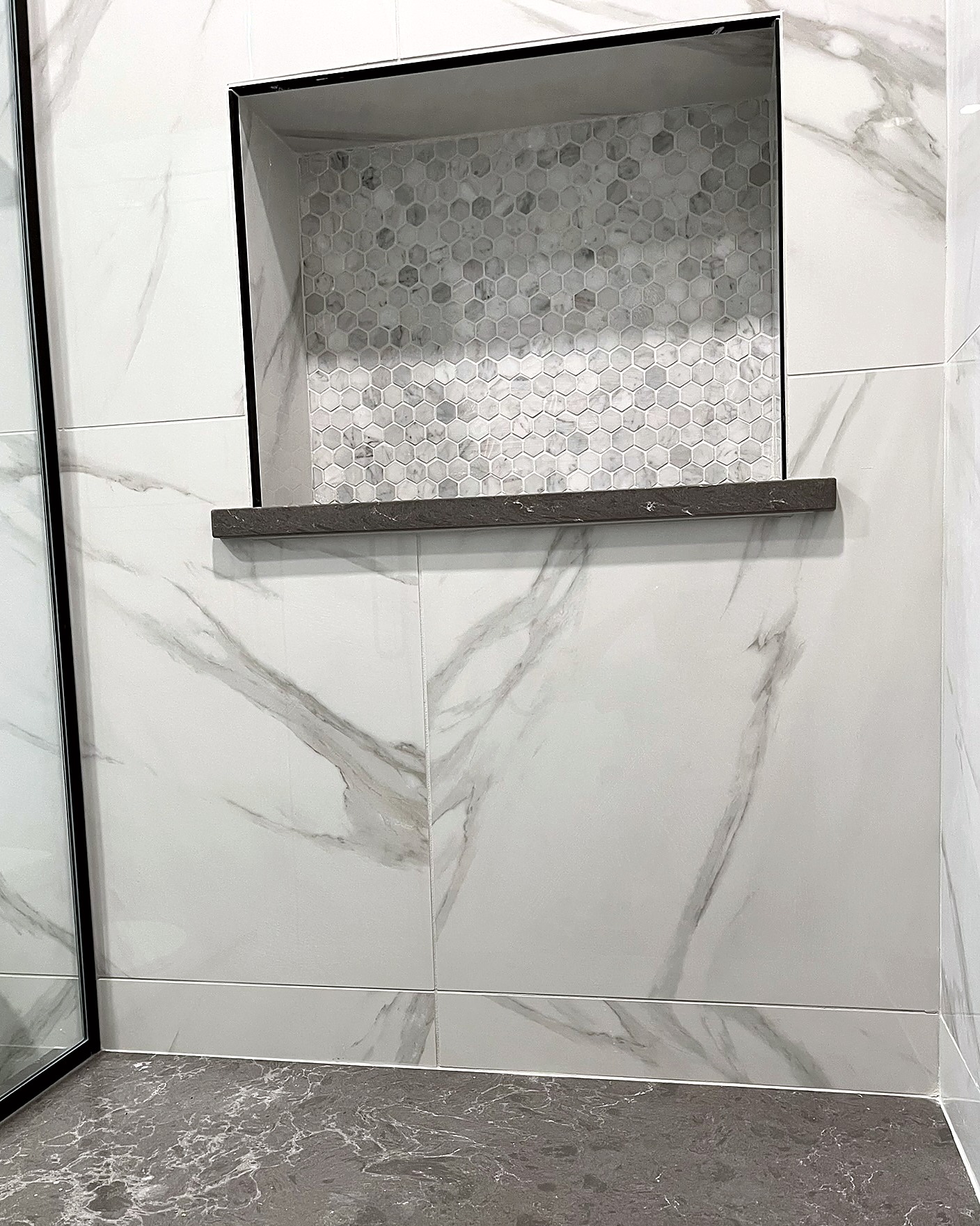 Walk-in shower with marble-pattern tile, a recessed niche, black fixtures, and a linear drain.